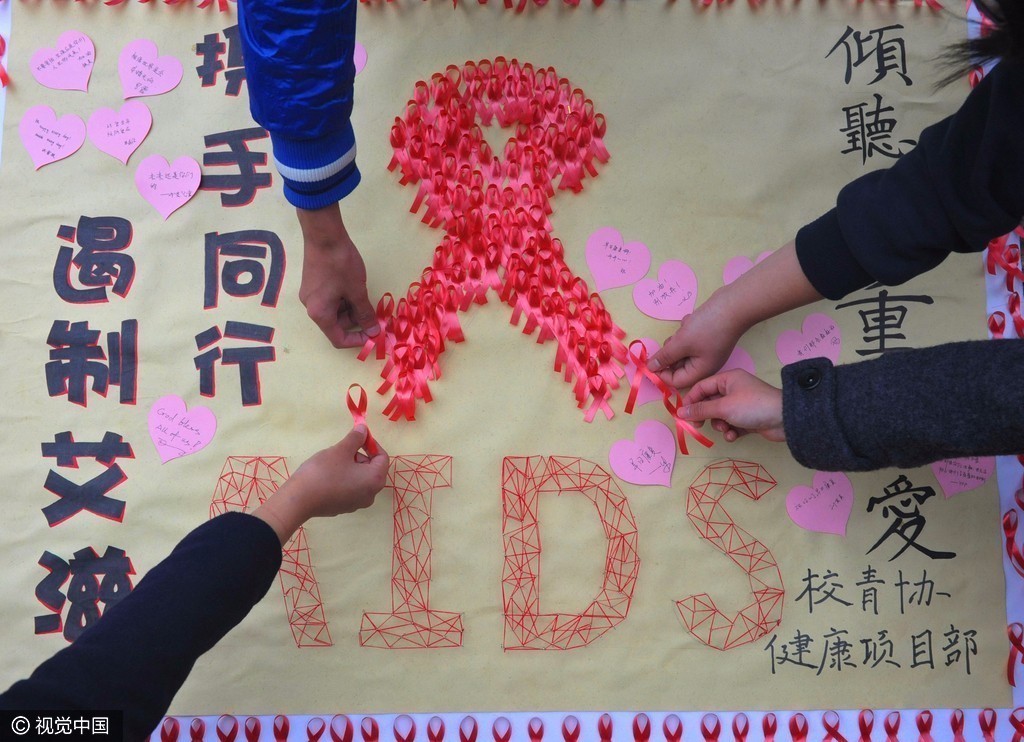 图为大学学生在世界艾滋病日主题宣传海报上粘贴红丝带.